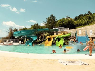 Scivoli d'acqua e bambini che giocano in una piscina all'aperto in una giornata di sole.