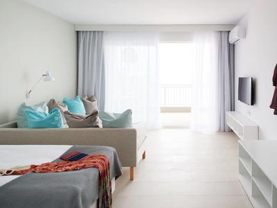 Camera d'albergo moderna e luminosa con letto, divano, TV e grande finestra con tende.