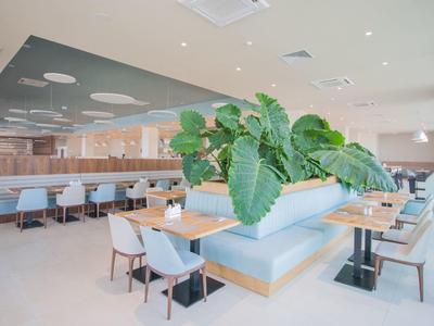 Sala da pranzo moderna e luminosa con tavoli, sedie e una grande pianta al centro.