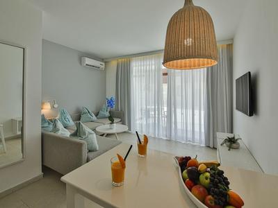 Soggiorno luminoso con divano, tavolo da pranzo, ciotola di frutta e TV a parete.