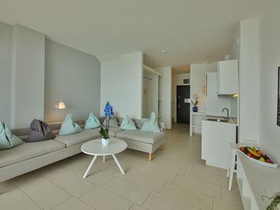 Soggiorno luminoso con divano, cuscini, tavolino rotondo e cucina aperta in un appartamento per vacanze.