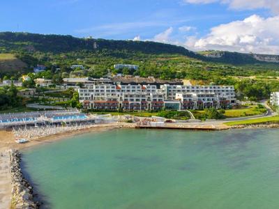 Hotel am Wasser mit Strand, grünem Hügel im Hintergrund und klarem Himmel