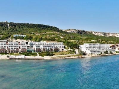 Costa con acqua limpida, spiaggia sabbiosa e hotel sotto un cielo azzurro.