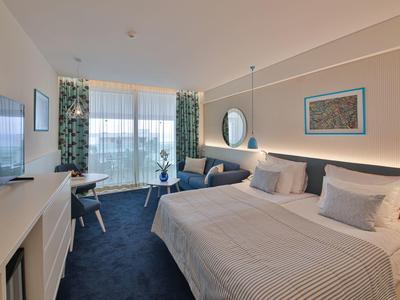 Camera d'hotel moderna con letto matrimoniale grande, zona salotto accogliente e vista sulla natura.