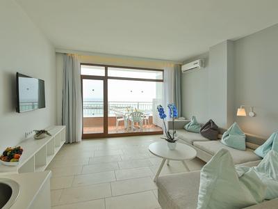 Soggiorno luminoso con divano, tavolino, TV e accesso al balcone con vista mare.