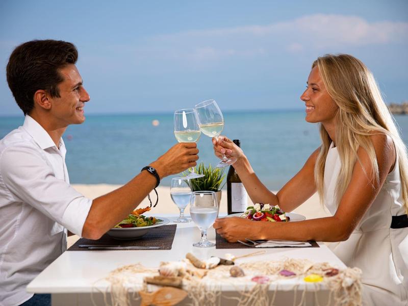 Una coppia brinda con bicchieri a un tavolo con vista mare.