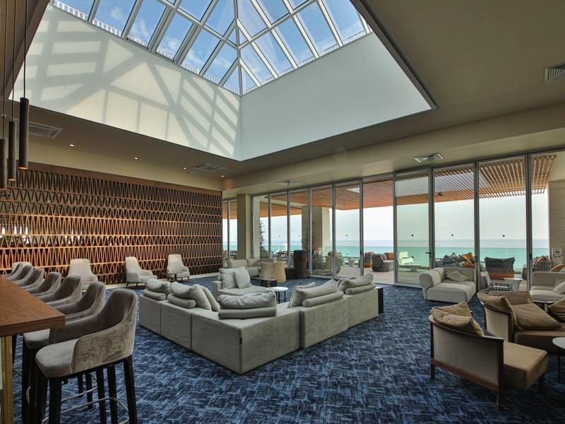 Lounge dell'hotel moderna con bar, divani e grande lucernario con vista sulla città.