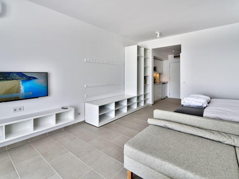 Stanza d'hotel luminosa arredata con TV, letto e zona soggiorno su pavimento piastrellato.