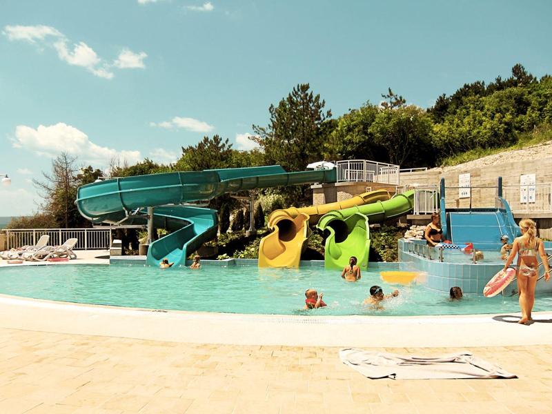 Scivoli d'acqua e bambini che giocano in una piscina all'aperto in una giornata di sole.