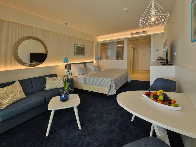 Camera d'hotel moderna con letto, divano e tavolo da pranzo con ciotola di frutta.