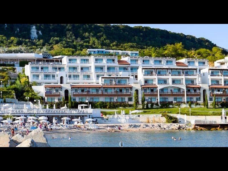 Zona giorno moderna con divano ad angolo grigio, tavoli bianchi e cucina aperta con zona pranzo.