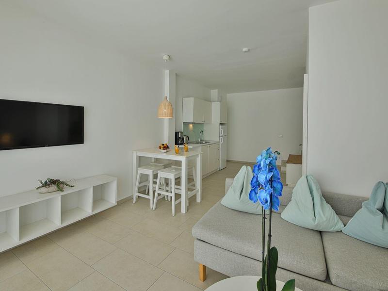 Soggiorno moderno con divano grigio, TV a parete e cucina aperta sullo sfondo.