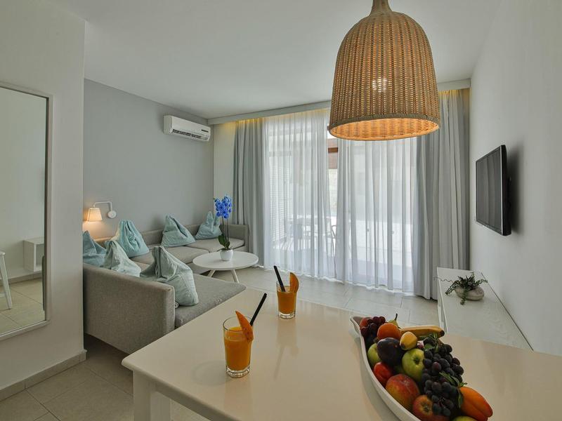 Soggiorno luminoso con divano, tavolo da pranzo, ciotola di frutta e TV a parete.