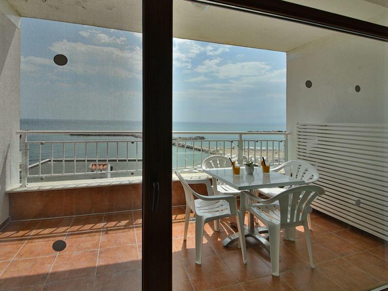 Tavolo in balcone con sedie bianche su terrazza vista mare sotto cielo nuvoloso.