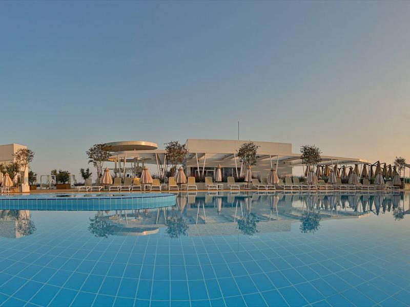 Ampia piscina con lettini e edificio moderno sullo sfondo al tramonto.