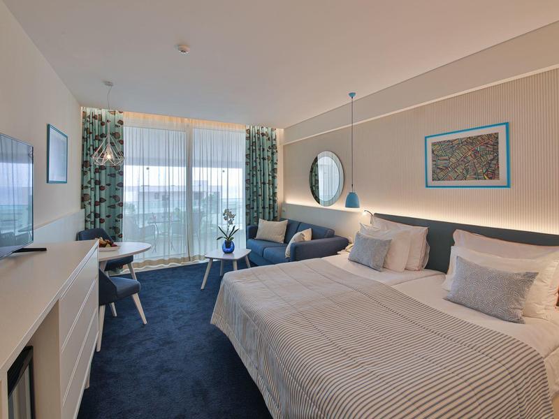 Camera d'hotel moderna con letto matrimoniale grande, zona salotto accogliente e vista sulla natura.