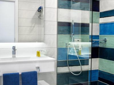 Salle de bain moderne avec lavabo blanc, serviettes bleues et cabine de douche aux carreaux rayés.