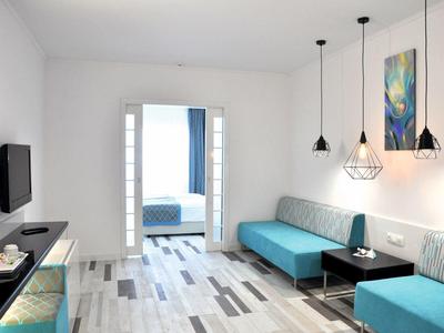 Espace séjour d'hôtel moderne avec canapés bleus, tables et vue sur la chambre.