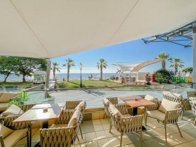 Terrasse avec chaises en osier et tables donnant sur jardin et mer à la plage.