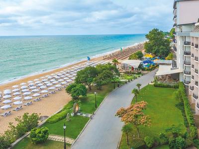 Vista de una playa con tumbonas, hotel adyacente y área de jardín.