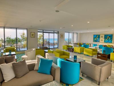 Salon d'hôtel lumineux et moderne avec fauteuils et canapés colorés, grandes fenêtres et vue sur la mer.