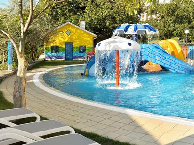 Piscine extérieure avec aire de jeux aquatique, toboggan et chaises longues dans le jardin de l'hôtel.