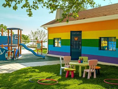 Colorido parque infantil con estructura para trepar y mesa con sillas frente a una casa arcoíris.