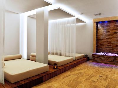 Salle de détente moderne avec lits longs, rideaux blancs et cascade décorative.