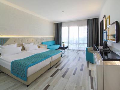 Chambre d'hôtel lumineuse avec deux lits simples, accents bleus et balcon avec vue sur la mer.