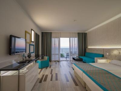 Chambre d'hôtel moderne avec lit, coin salon et vue sur la mer par de grandes fenêtres.