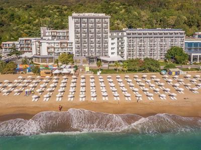 Grand hôtel à plusieurs étages sur la plage avec de nombreux parasols blancs et chaises longues devant.