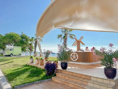 Área exterior soleada con terraza, plantas y molino de viento en un entorno hotelero tropical.