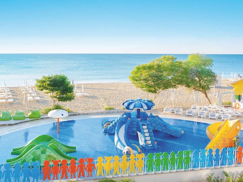 Aire de jeux colorée pour enfants avec piscine et toboggans sur la plage face à la mer.