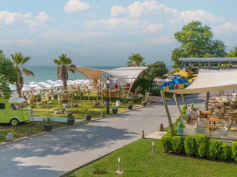 Espace jardin verdoyant avec sièges, vue sur la mer et bâtiments d'hôtel en arrière-plan.