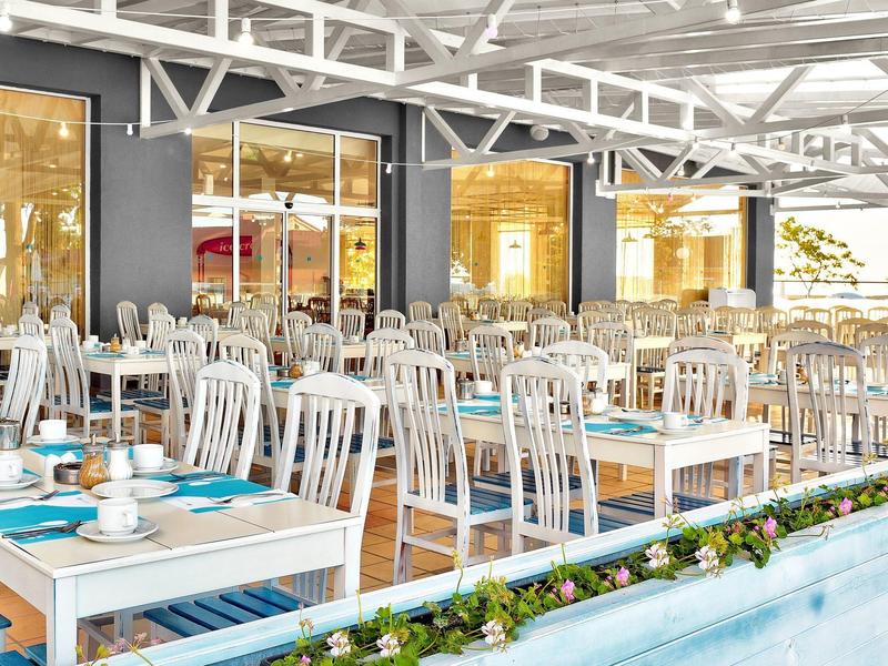 Restaurant extérieur lumineux avec chaises et tables blanches, vue sur un bassin d'eau.