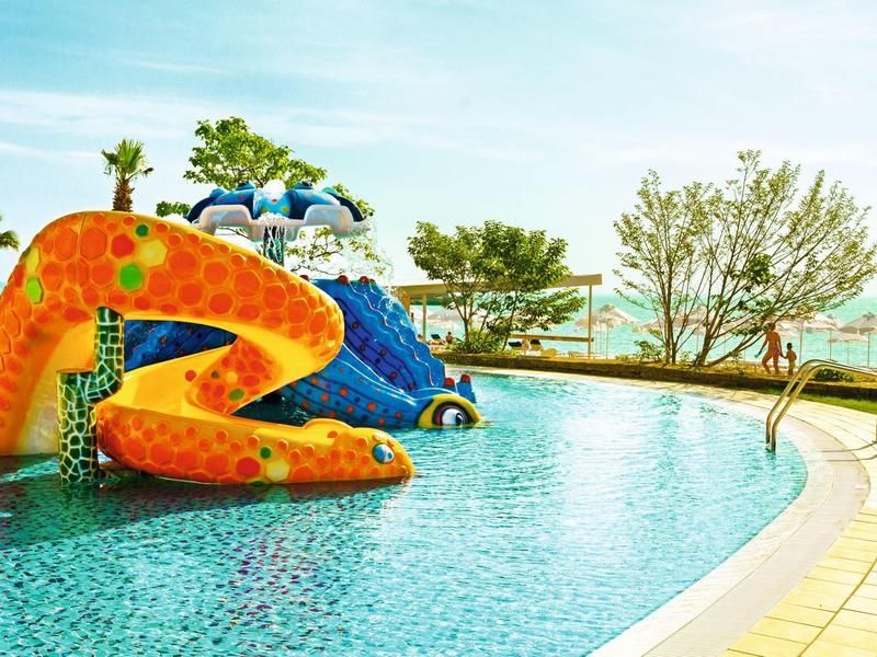 Piscine intérieure avec toboggan coloré ludique et arbres environnants.