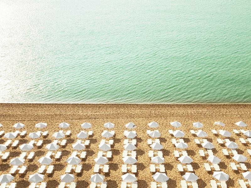 Plage avec parasols blancs disposés régulièrement et eau verte calme.