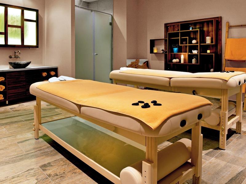 Salle de massage confortable avec deux tables en bois et éclairage chaleureux.