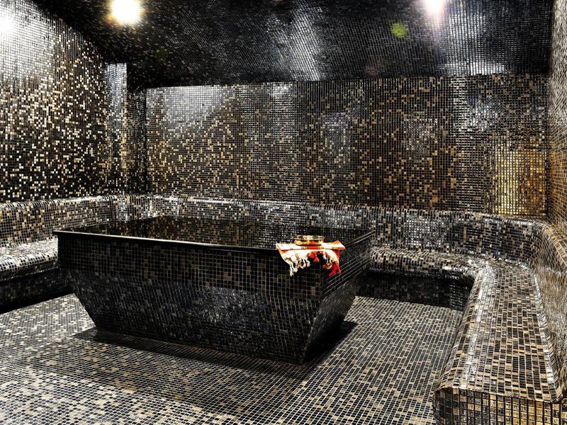 Espace spa sombre avec un jacuzzi et des carreaux de mosaïque, décoré de serviettes.