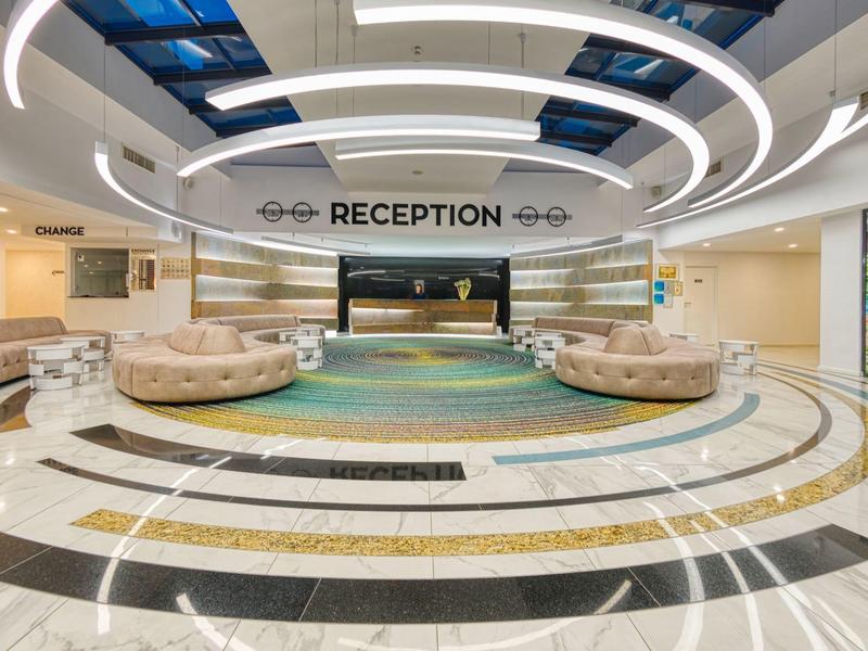 Hall d'hôtel moderne avec zones de sièges circulaires et réception élégante sous des luminaires circulaires.
