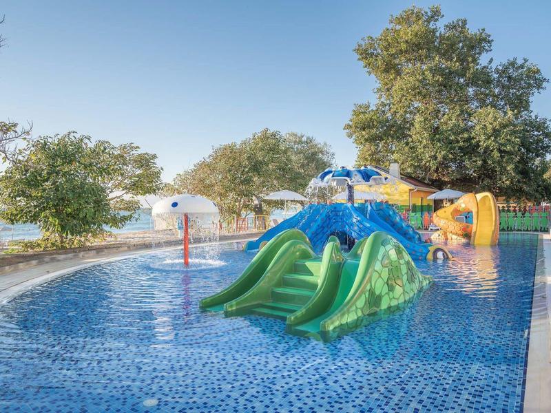 Bassin pour enfants avec toboggans colorés et arbres en arrière-plan sous un ciel clair.