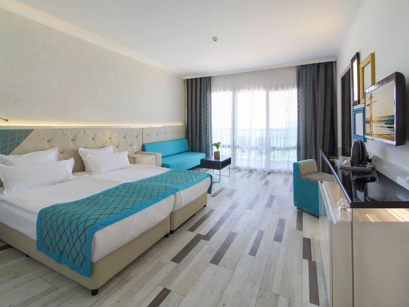 Chambre d'hôtel lumineuse avec deux lits simples, accents bleus et balcon avec vue sur la mer.