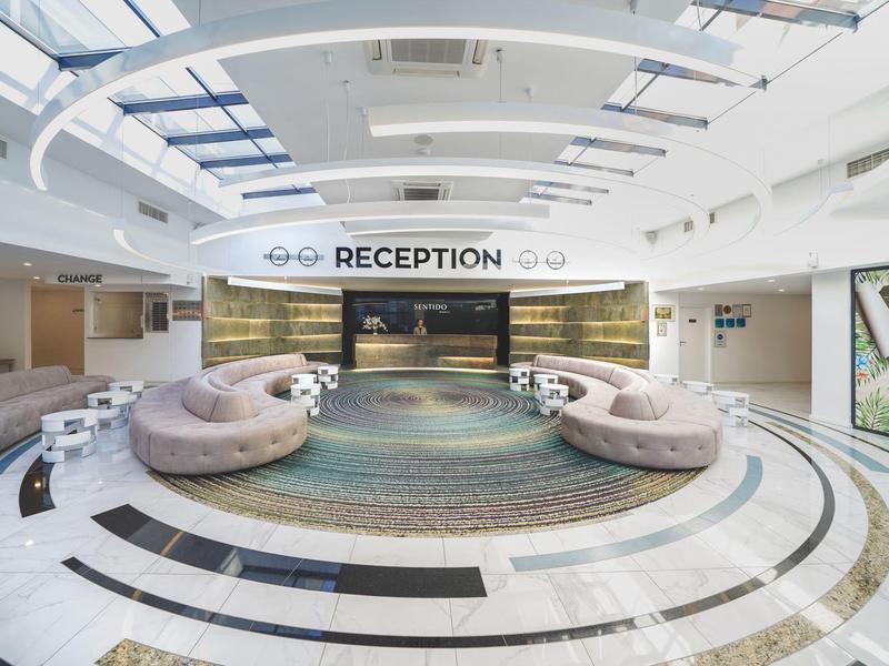 Hall d'hôtel lumineux avec canapés courbés et grand comptoir de réception sous un plafond en verre