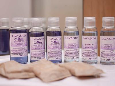 Zeven kleine flesjes lavendel douchegel op een rij met enkele beige zeepstukken ervoor.