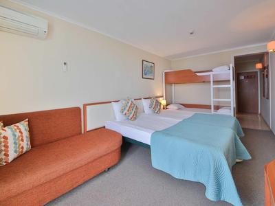 Hotelkamer met tweepersoonsbed, stapelbed, bank en airconditioning.