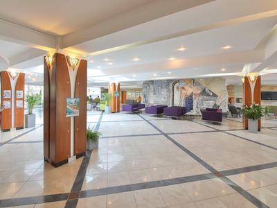 Ruim hotel lobby met marmeren vloer, zithoeken en grote zuilen.