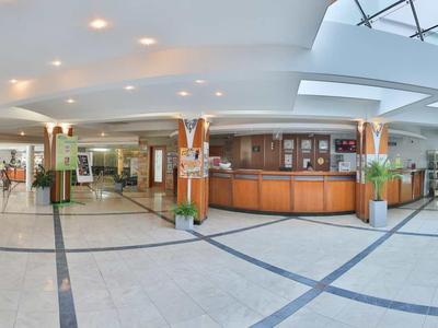 Grote heldere hotel lobby met receptie, zithoeken en glazen koepel.