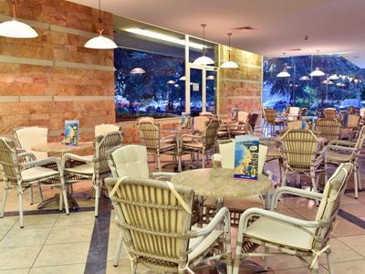 Gemütlicher Essbereich mit vielen Stühlen und Tischen, helle Innenbeleuchtung und große Fenster mit Blick nach draußen.