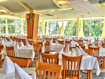 Heller Speisesaal mit Holzstühlen und weißen Tischdecken, umgeben von großen Fenstern.