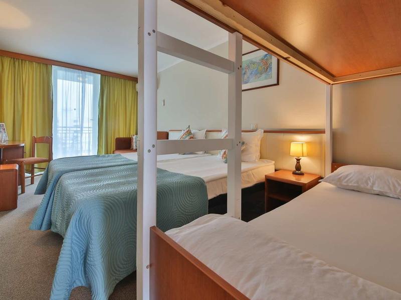 Hotelkamer met twee eenpersoonsbedden, bureau en raam met groene gordijnen.